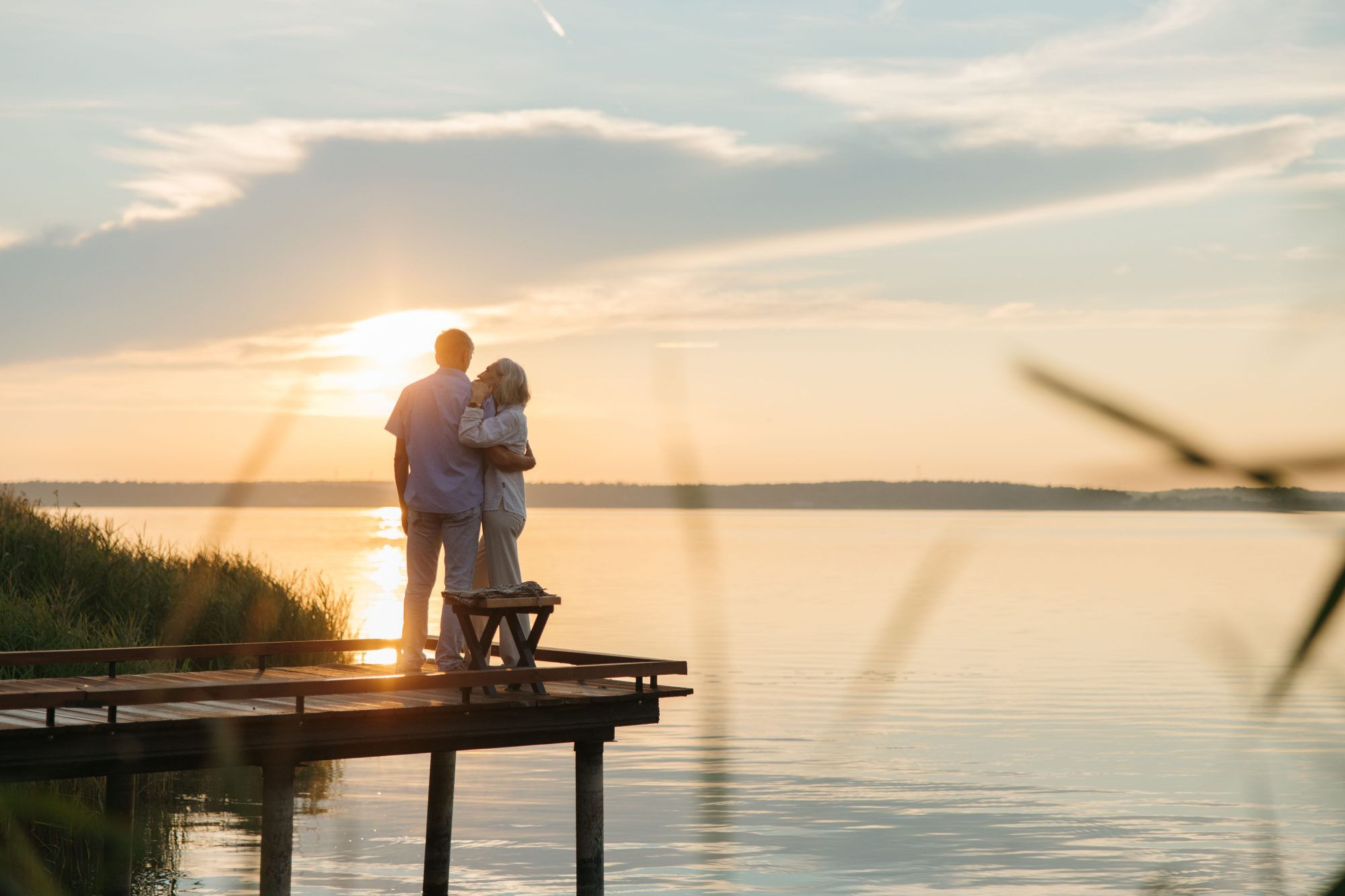 A retired couple watching the sunset together from a lakeside dock